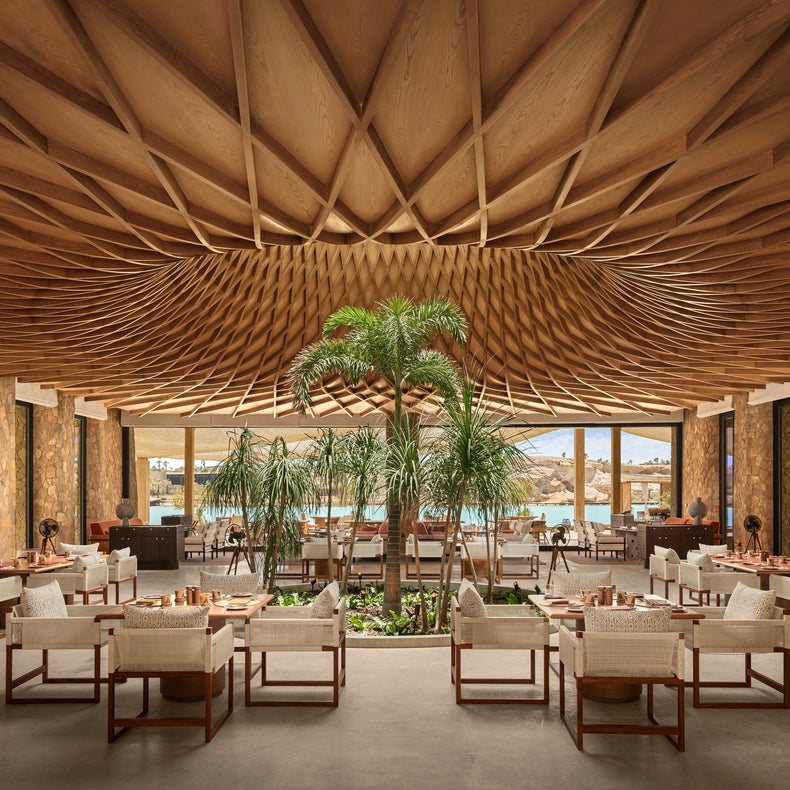 Restaurant featuring wood ceiling accents, natural indoor greenery, textured seating, and expansive windows with views of water and rugged hills.