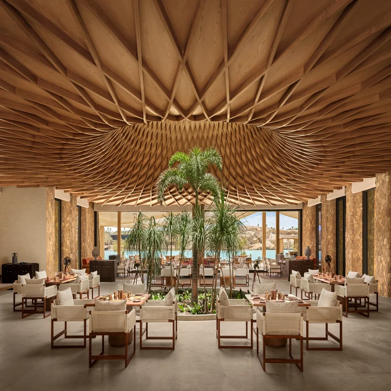 Restaurant featuring wood ceiling accents, natural indoor greenery, textured seating, and expansive windows with views of water and rugged hills.