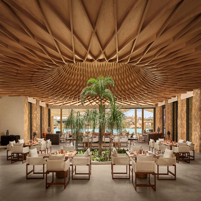 Restaurant featuring wood ceiling accents, natural indoor greenery, textured seating, and expansive windows with views of water and rugged hills.