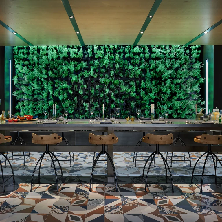 Dining area featuring a long wooden table, contemporary chairs, patterned tile flooring, wall shelving with jars, and a vibrant vertical garden accent.