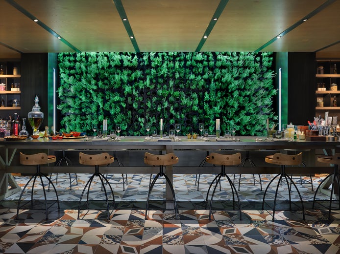 Dining area featuring a long wooden table, contemporary chairs, patterned tile flooring, wall shelving with jars, and a vibrant vertical garden accent.