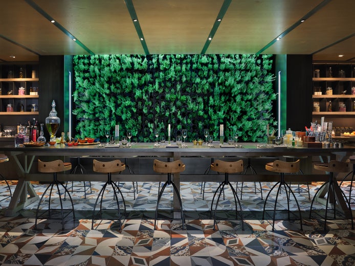Dining area featuring a long wooden table, contemporary chairs, patterned tile flooring, wall shelving with jars, and a vibrant vertical garden accent.