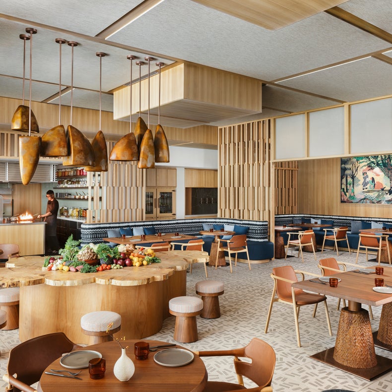 مطعم بكراسي خشبية، وطاولة على شكل جذع شجرة، وأضواء معلّقة، ومقاعد مبطنة زرقاء، ولوحات جدارية جدارية، وطاولات مرتبة لتناول الطعام في أجواء ترحيبية.