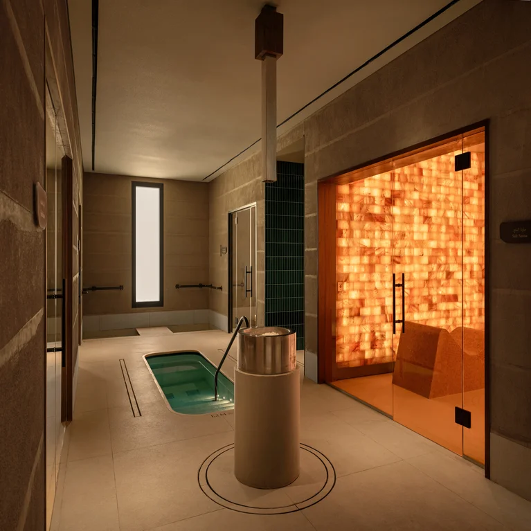 Spa room featuring a small pool, circular metal fountain, neutral stone walls, and an illuminated salt cave sauna with accessible glass doors.