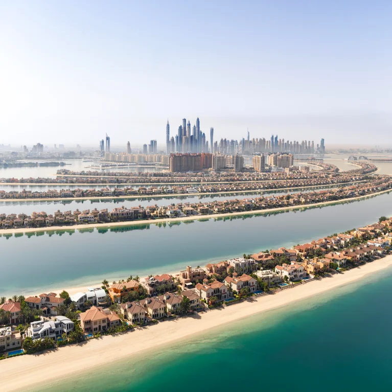 Palm Jumeirah’s palm-shaped islands with villas, gentle shoreline, and distant city skyline meet the clear water and sandy beaches of Dubai.