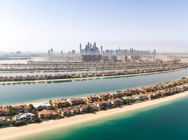 Palm Jumeirah’s palm-shaped islands with villas, gentle shoreline, and distant city skyline meet the clear water and sandy beaches of Dubai.