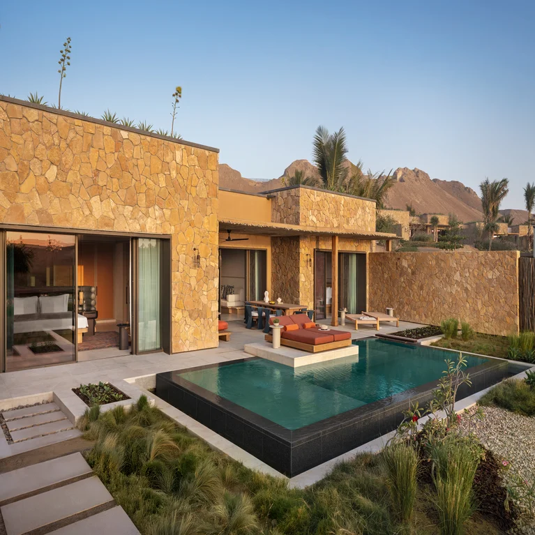 Serene stone building with expansive windows, pool, accessible pathways, comfortable seating, gardens, mountain views and open sky promote a sense of peace and connection to nature.