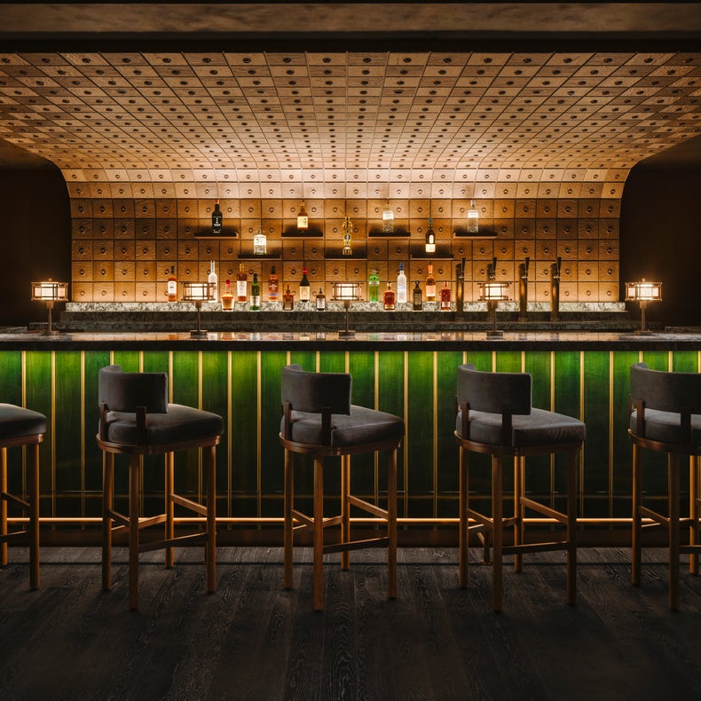 تتميز منطقة البار بخمسة مقاعد للبار، ومنضدة خضراء مضاءة بهدوء، وجدار خلفي من الزجاجات ذات الألواح المربعة المتوهجة؛ إضاءة دافئة تضمن الراحة البصرية.