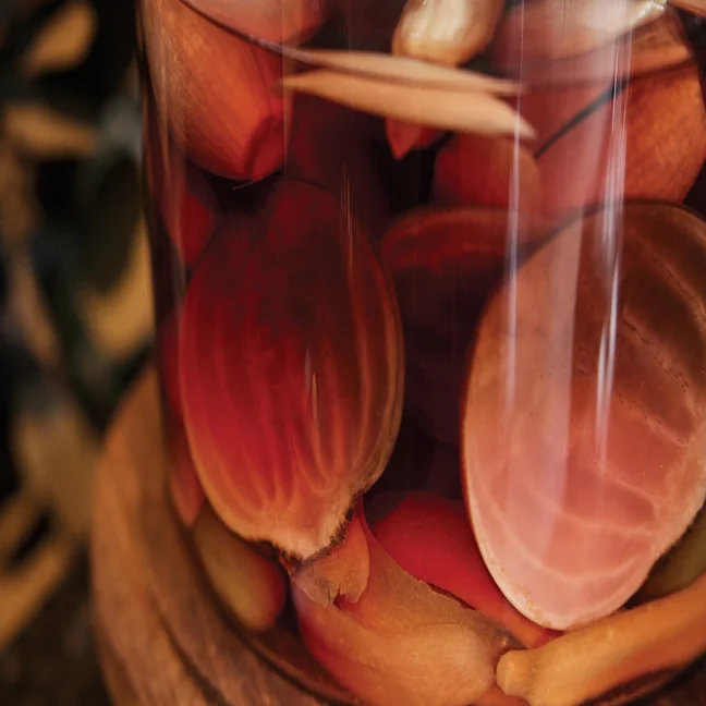 Sliced beets and carrots in a glass jar of pickling liquid rest on a wooden surface, highlighting vibrant colors and fresh preservation.
