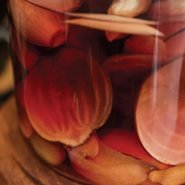 Sliced beets and carrots in a glass jar of pickling liquid rest on a wooden surface, highlighting vibrant colors and fresh preservation.
