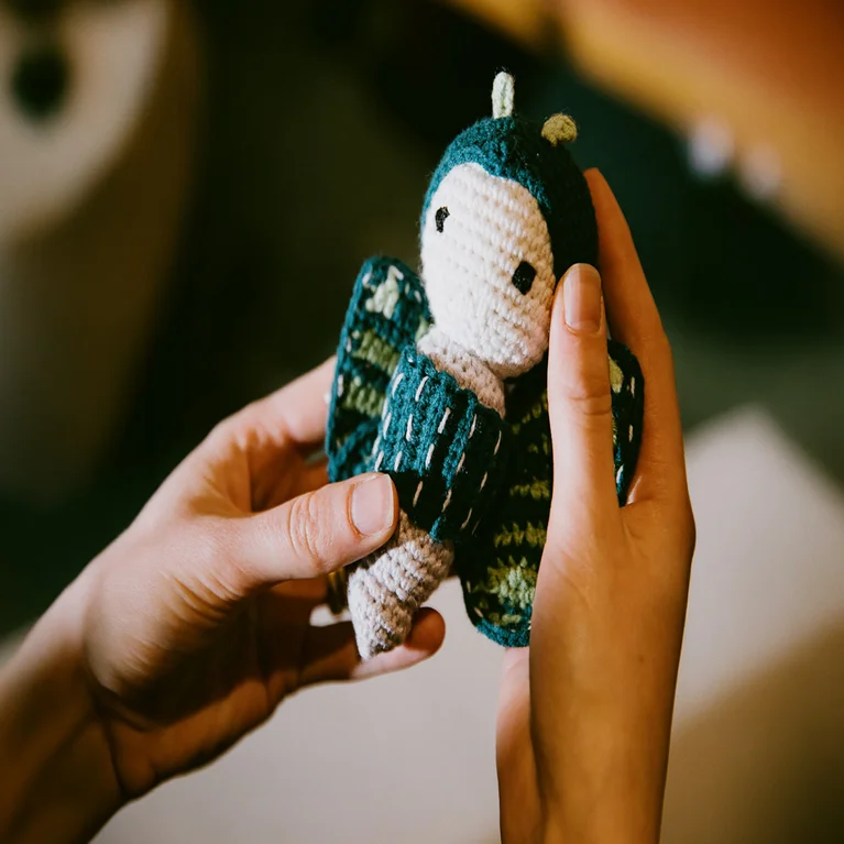 Crocheted bird doll featuring a teal and white body, green wings, and a white face, held gently to showcase thoughtful craftsmanship.