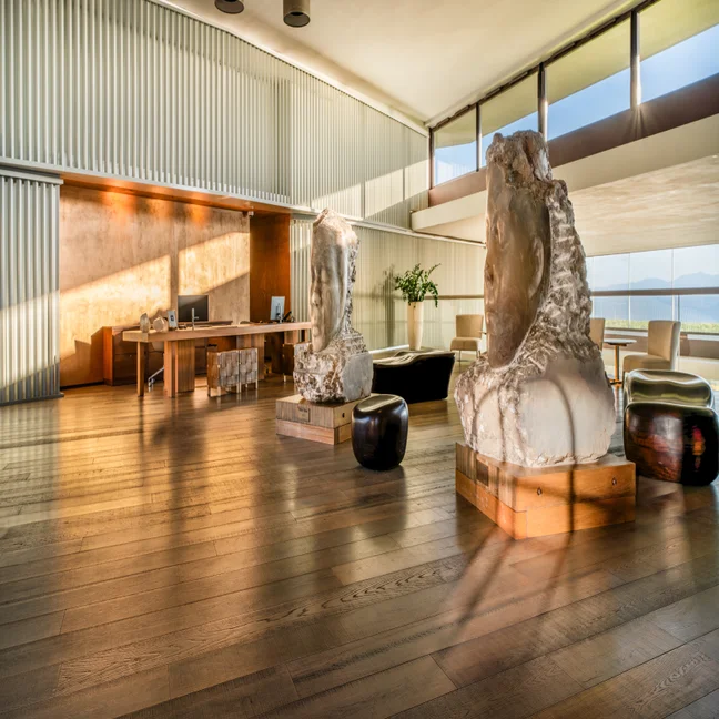 Office featuring large windows, wooden flooring, desk area, and two stone busts. Ample natural light enhances a calm, inviting workspace designed with wellness in mind.