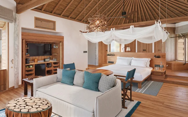 A suite featuring a vaulted wood ceiling, canopy bed, sofa with teal pillows, and a coffee table crafted from wood slices.