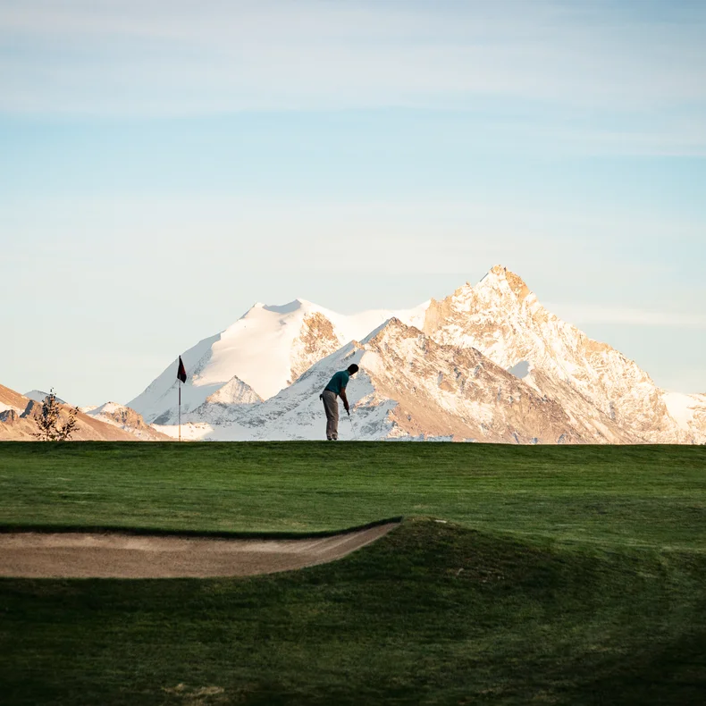 A guest enjoys a round of golf on a well-kept green, framed by snow-capped mountains and open sky, highlighting harmony with the surrounding landscape.