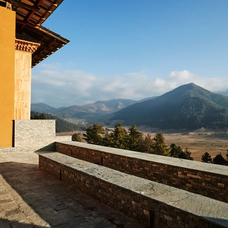 一座石墙建筑坐落在群山和森林旁,映衬着晴朗的天空,突出了天然材料和周围的景观。.