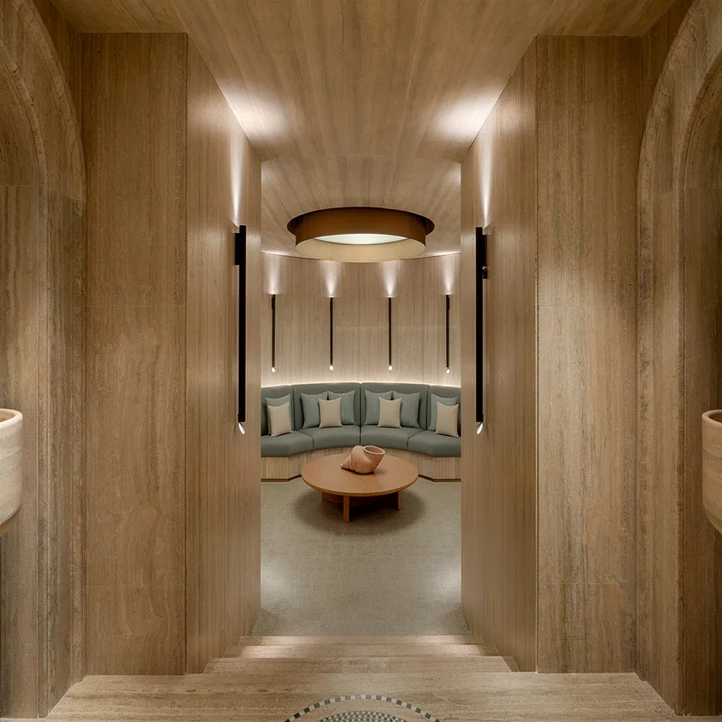 Lounge with timber walls, soft ambient light, a curved sofa and round coffee table at the center; designed for comfort and sustainable materials.