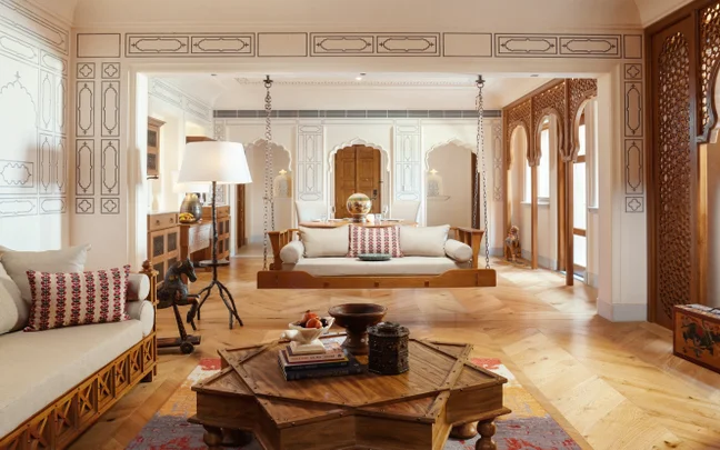 Serene living area featuring Indian craft details, carved wood panels, two suspended wooden swings, textured cushions, and a geometric wood coffee table.