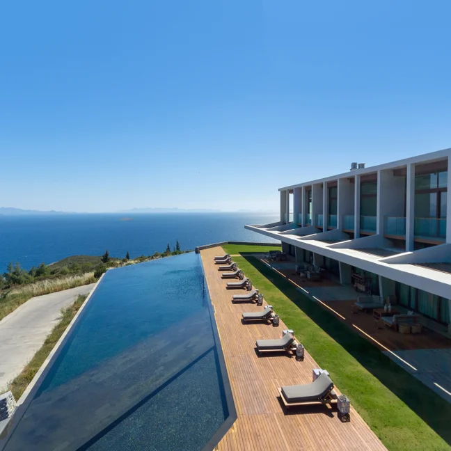 Eco-conscious hotel with infinity pool facing the ocean, lounge chairs on a wooden deck, and open sky, reflecting Six Senses’ wellness and sustainability focus.