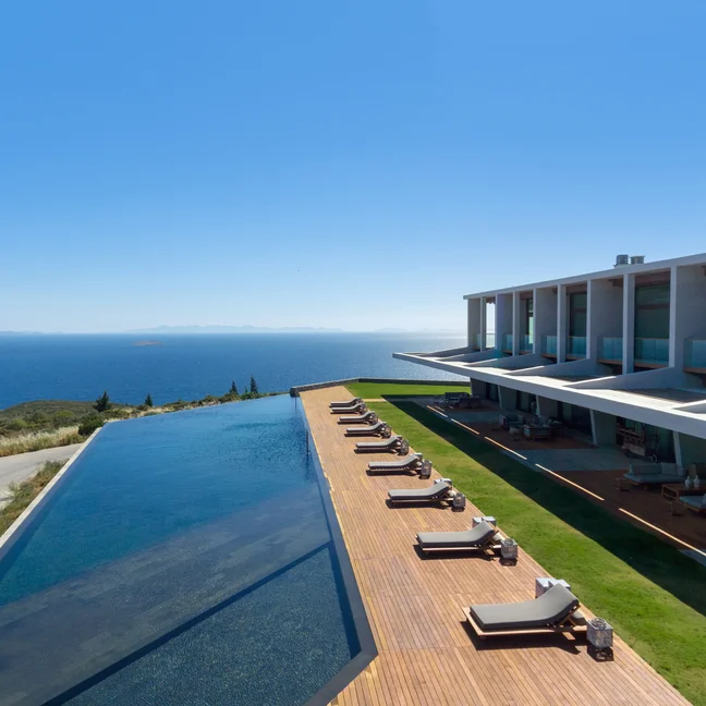 Eco-conscious hotel with infinity pool facing the ocean, lounge chairs on a wooden deck, and open sky, reflecting Six Senses’ wellness and sustainability focus.
