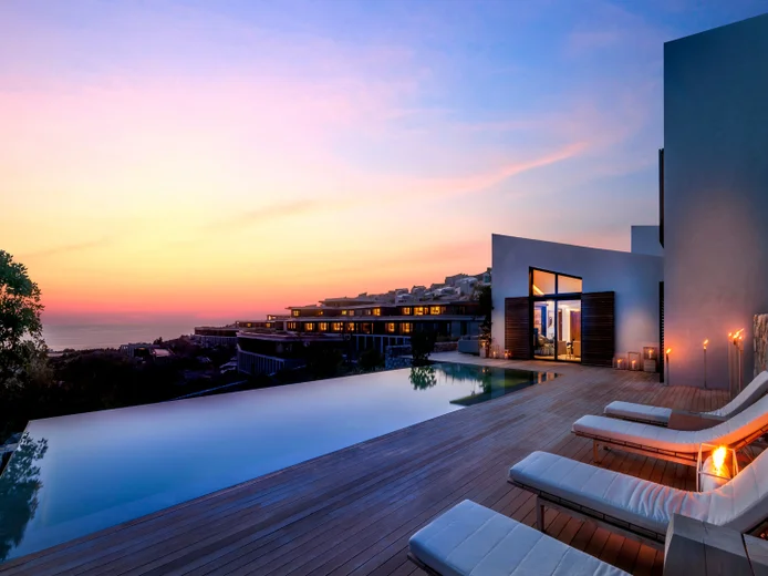 Poolside seating on a wooden deck, set against modern city architecture and a vibrant sunset, designed for comfort and mindfully integrated with the urban environment.