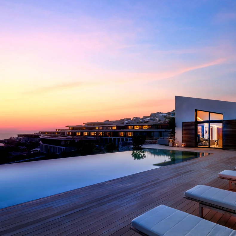 Poolside seating on a wooden deck, set against modern city architecture and a vibrant sunset, designed for comfort and mindfully integrated with the urban environment.