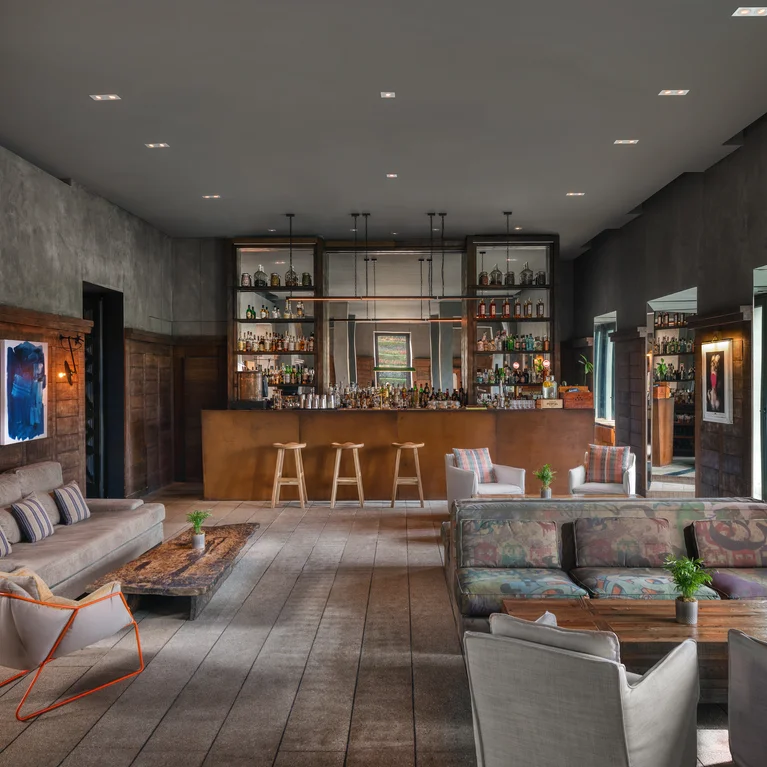 بار ومنطقة جلوس مصنوعة من مواد طبيعية، مع أريكة مريحة وإضاءة دافئة، مما يشجع على الاسترخاء في أجواء هادئة.