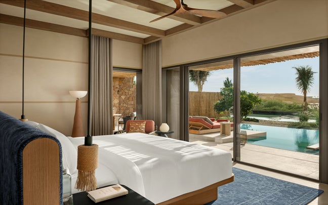 Bedroom featuring a spacious bed, access to a private pool through sliding glass doors, outdoor lounge chairs, palm trees, desert views, and natural modern decor.