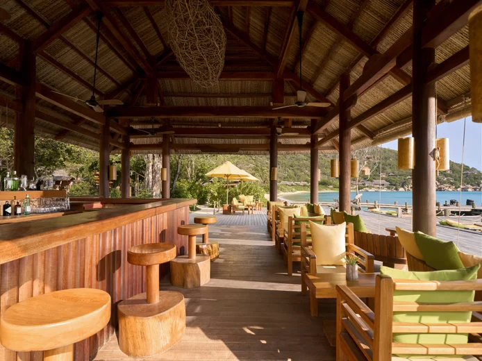 Wooden bar counter with stools and lounge chairs facing the beach and ocean.