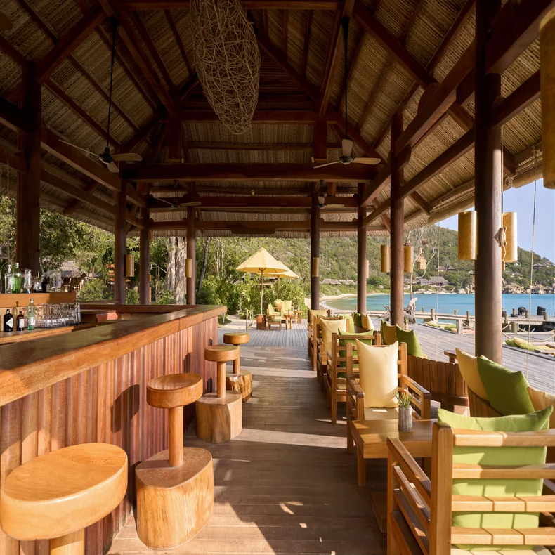 Wooden bar counter with stools and lounge chairs facing the beach and ocean.