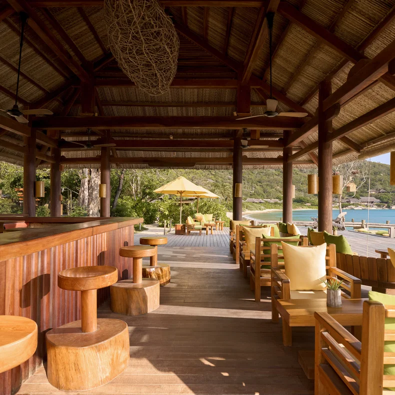 Wooden bar counter with stools and lounge chairs facing the beach and ocean.