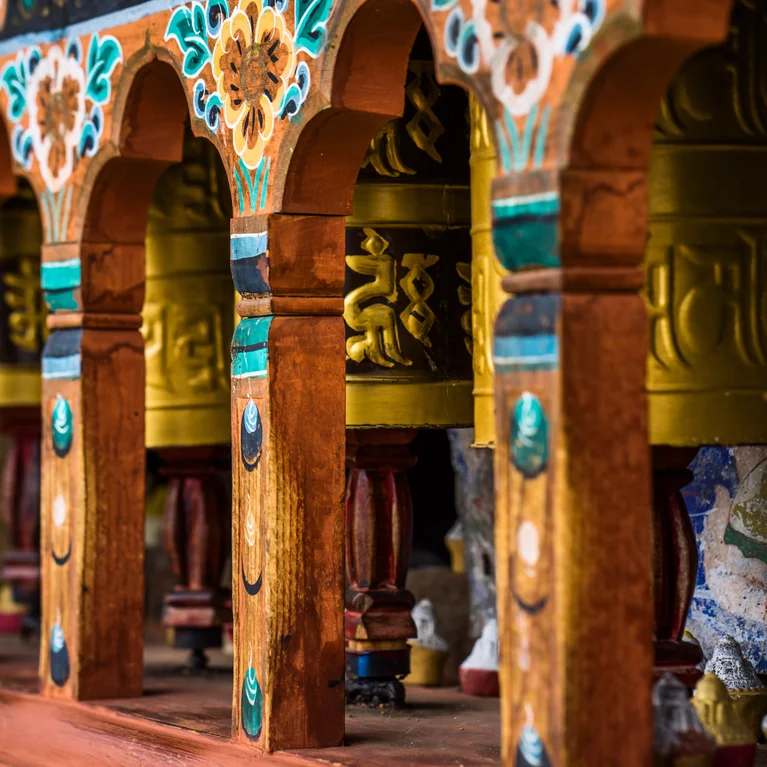 在雕刻木拱门的衬托下,带有细致多彩图案的祈祷轮一字排开,体现了佛教传统和精湛工艺。.