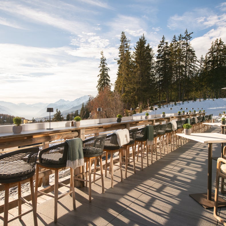 Le patio, équipé de tables et de chaises en bois, offre une vue sur les montagnes enneigées et les pins ; certaines tables sont équipées de couvertures pour plus de confort.