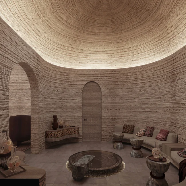 Circular space features textured walls, an arched doorway, curved sofa, small tables and cushions in a serene, nature-inspired setting with gentle lighting.