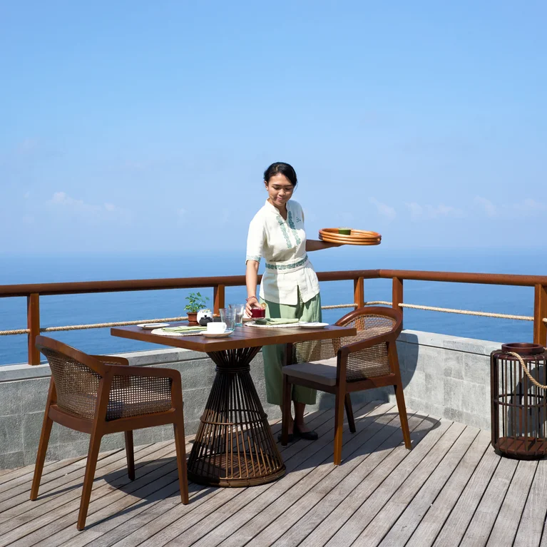 تم تأثيث السطح الخشبي المواجه للبحر بطاولة وكرسيين وطاولة جانبية صغيرة، يغمرها الضوء الطبيعي تحت سماء صافية.