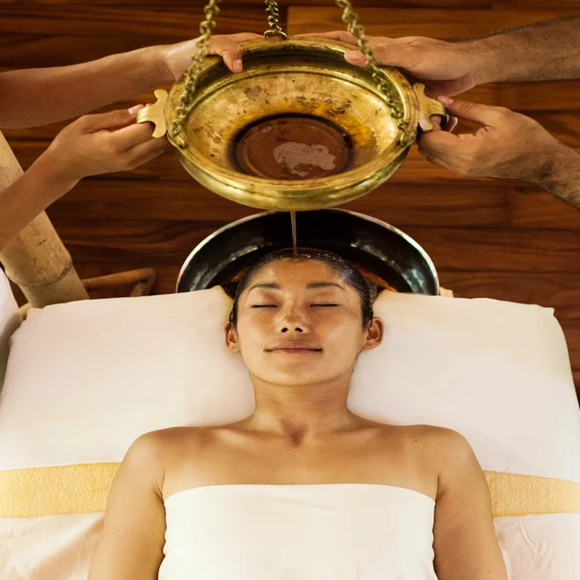 Guest enjoys a gentle oil flow onto the forehead during a holistic wellness treatment, emphasizing relaxation and traditional technique in a calm spa setting.