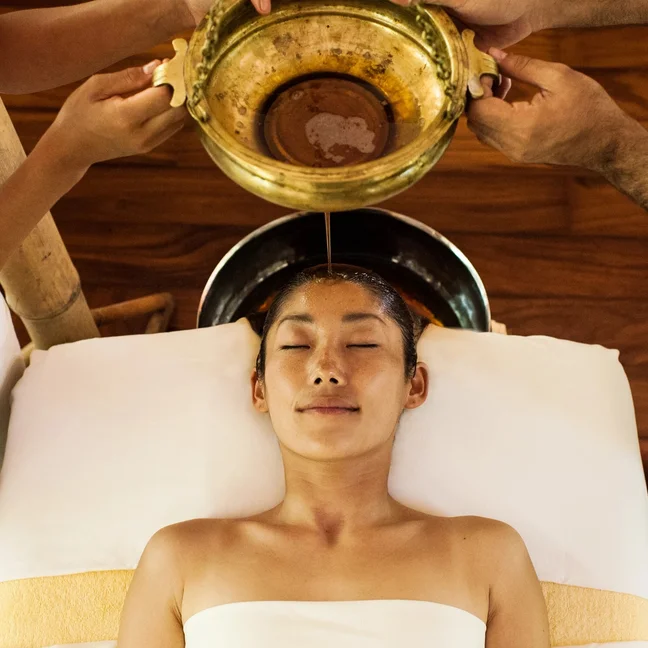 Guest enjoys a gentle oil flow onto the forehead during a holistic wellness treatment, emphasizing relaxation and traditional technique in a calm spa setting.