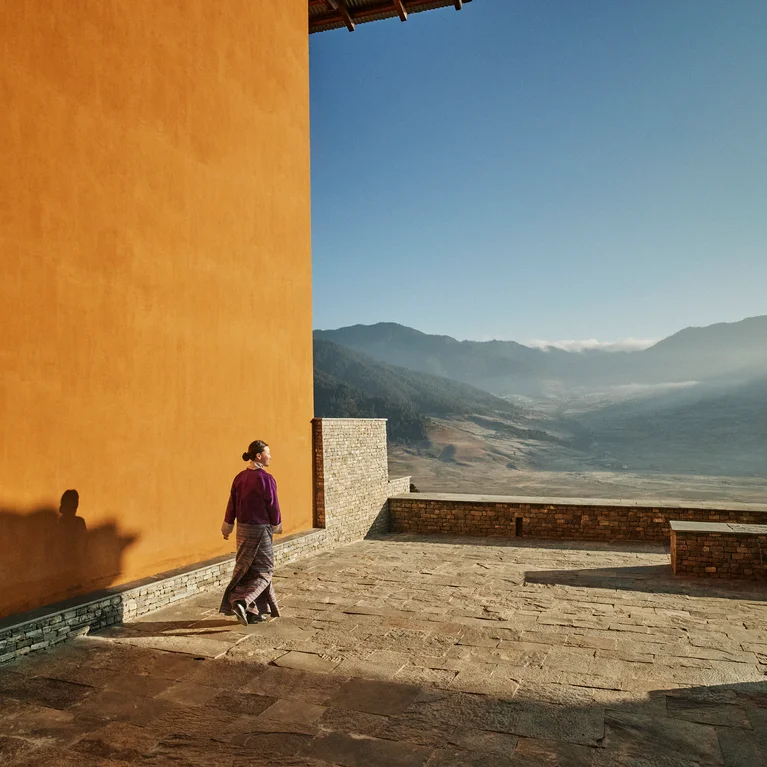 一位客人漫步在橘黄色墙面的石头露台上,俯瞰着湛蓝天空下宁静的山谷。.