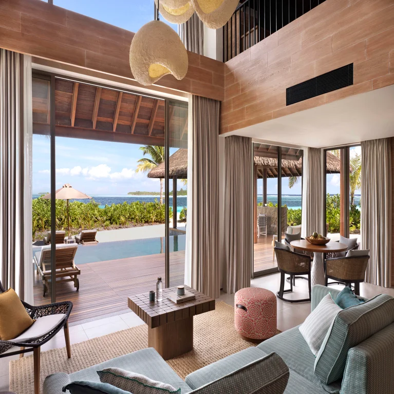Suite with expansive windows, natural materials, spacious seating and dining areas; overlooks a private pool, sun loungers, lush palms and the ocean.