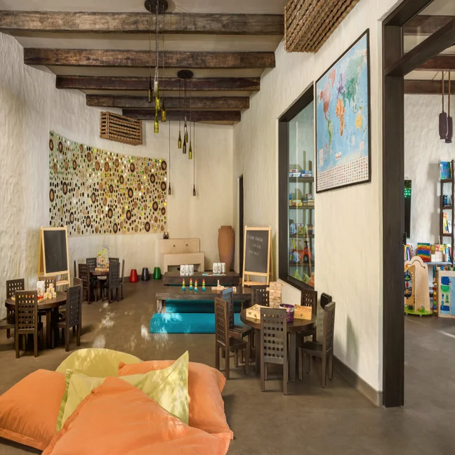 Children’s activity room featuring wooden tables, play areas, a wall-mounted world map, and pendant lights made from glass bottles.
