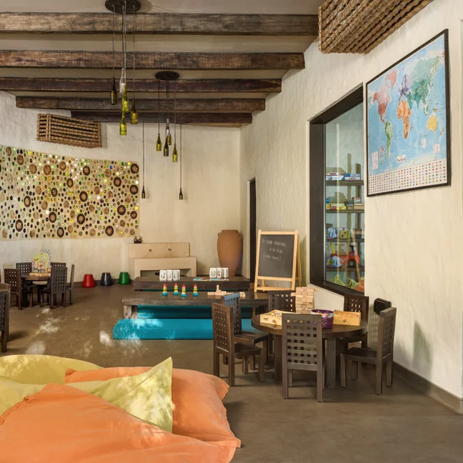 Children’s activity room featuring wooden tables, play areas, a wall-mounted world map, and pendant lights made from glass bottles.