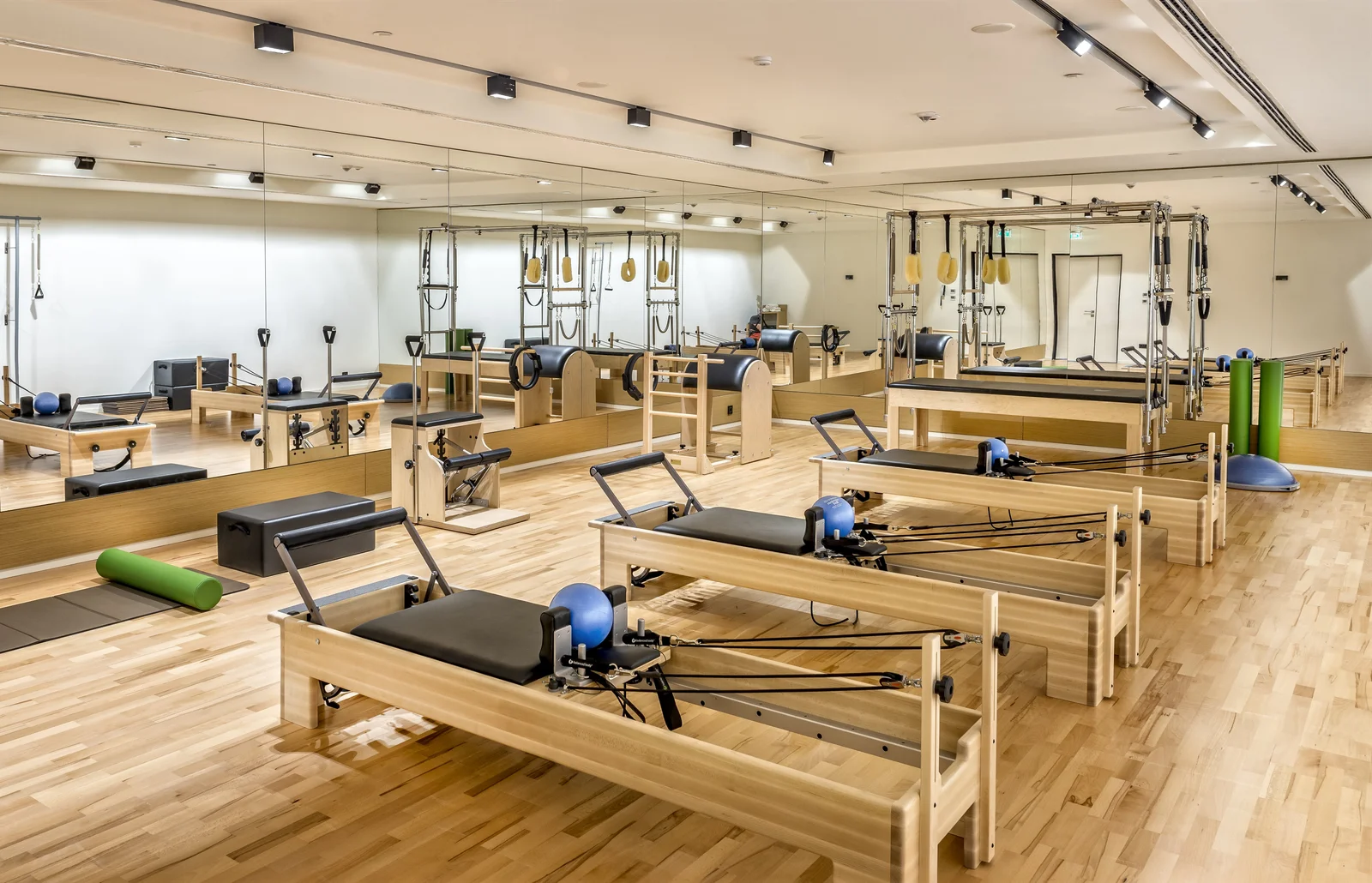 A pilates studio in pale wood with a mirrored wall, six reformers spaced across the floor and a rack of small equipment at the side.
