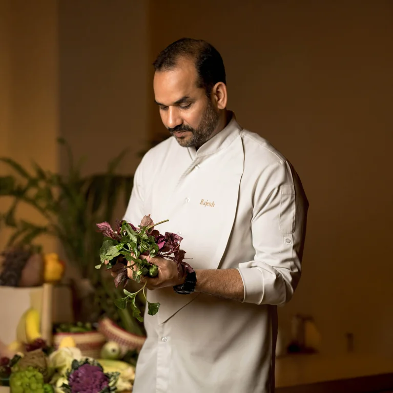 A person preparing fresh greens, surrounded by an array of vegetables and plants, reflecting a commitment to wellness and sustainable sourcing.