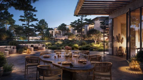 Outdoor dining area with a wooden table prepared for a meal, set amid green gardens and modern buildings at sunset. Gentle lighting enhances comfort and ambiance.