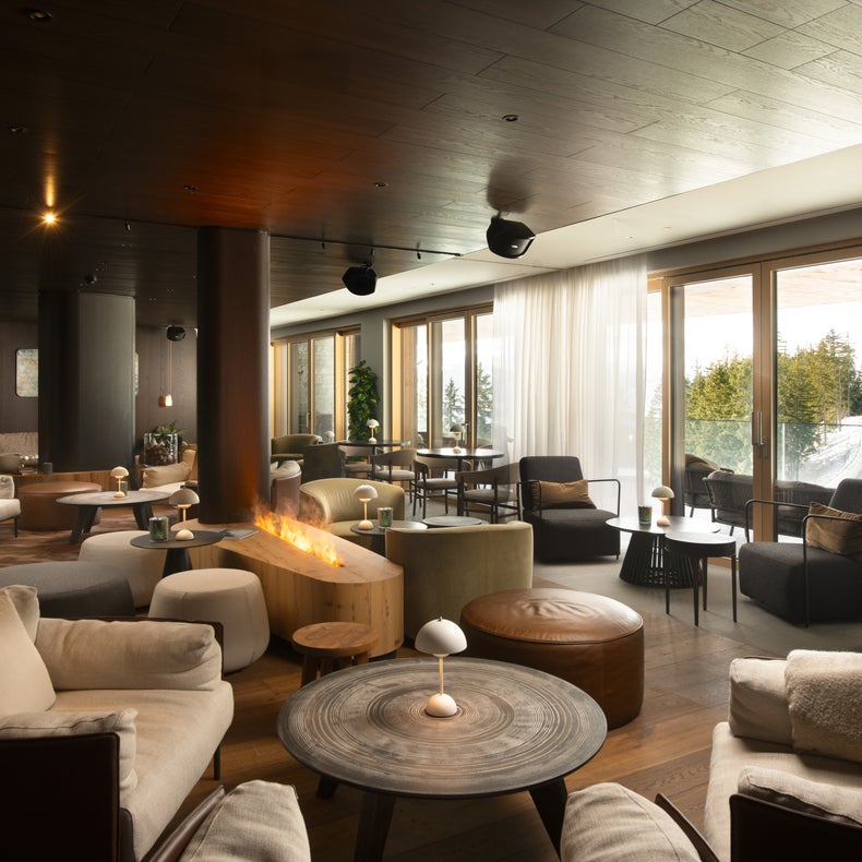 Le coin salon est composé d'un canapé aux tons naturels, d'une table basse en bois organique, d'une lampe suspendue et d'un mur d'accentuation sombre avec un ensemble de décorations circulaires blanches pour l'équilibre sensoriel.