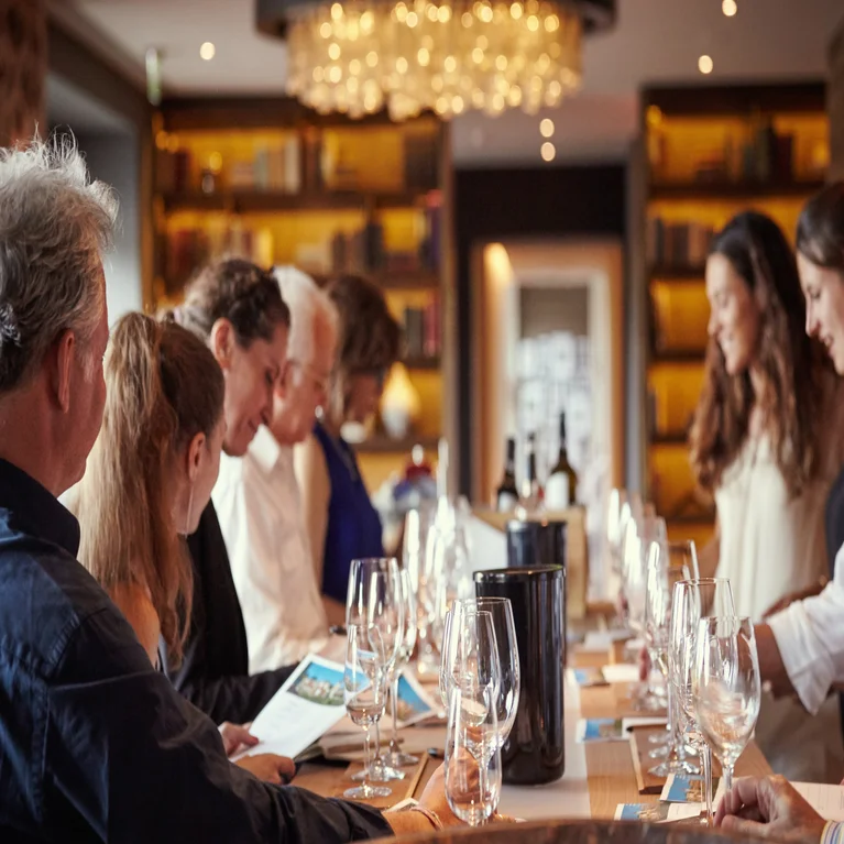 Guests gather at the table with wine glasses, menus and bottles under warm lighting in an inviting and carefully designed dining area.