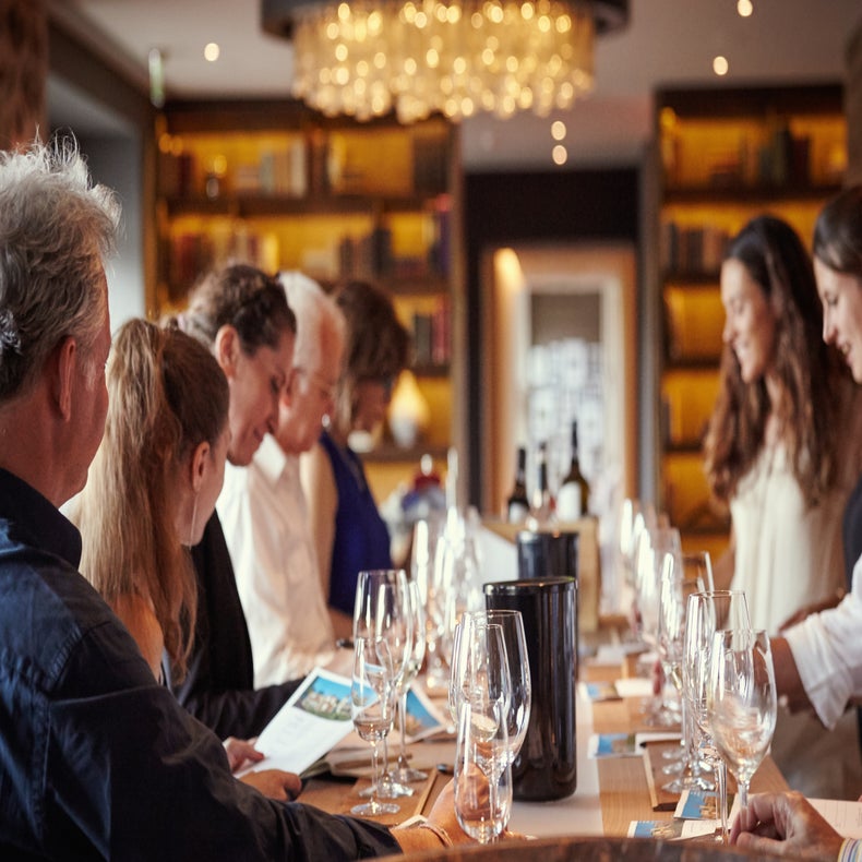 Guests gather at the table with wine glasses, menus and bottles under warm lighting in an inviting and carefully designed dining area.
