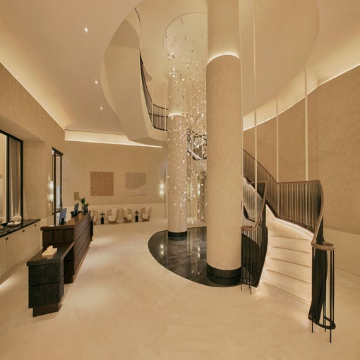 Hotel lobby featuring a curved staircase, contemporary lighting, earthy colors, comfortable seating areas, and warm ambient illumination.