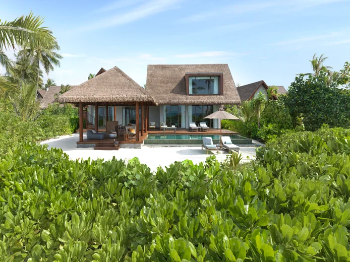Villa with natural thatch roof, private pool, sun loungers, and garden plants, designed for privacy and well-being, set beneath a clear blue sky.
