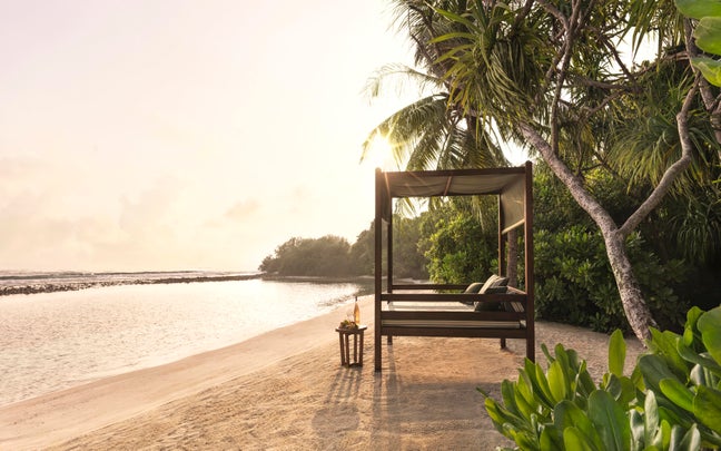 A thoughtfully placed bed overlooks the shoreline, inviting restful sleep close to nature with gentle waves and soft sand enhancing a sense of wellbeing.