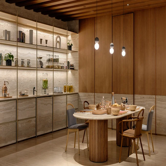 Kitchen with natural wood and stone finishes, open shelves with curated objects and greenery, dining table set for a meal beneath pendant lights.
